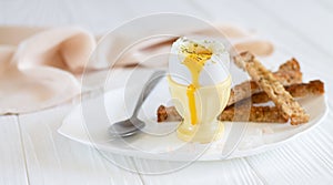 Soft boiled egg in white plate with toast and spoon for breakfast