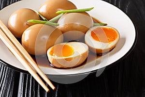 Soft-boiled eggs of nitamago in soya marinade with green onions close-up in a plate. horizontal photo