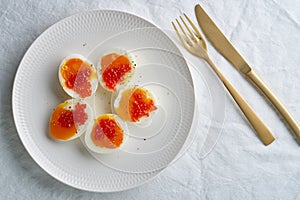 Soft-boiled eggs, peeled and cut into two halves, and salmon caviar lying on white plate.