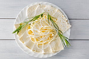 Soft cheese Chechil and Guda on plate with herbs on wooden table. Top view