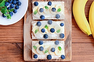 Soft cheese cream, bananas, mint and berries sandwiches. Vegetarian diet sandwiches crispbread on wooden board. Top view