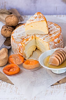 Soft cheese with cut off slice creamy texture, orange rind with mold, French, German, Alps, honey dipper, walnuts, dried apricots,