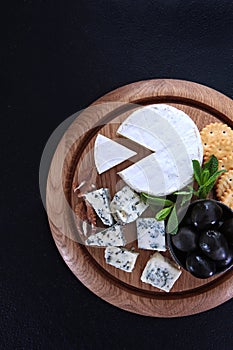 Soft cheese with white mold on a round wooden board. Camembert and blue-mildewed cheese. Cheese plate. Flat layout. Top view. A