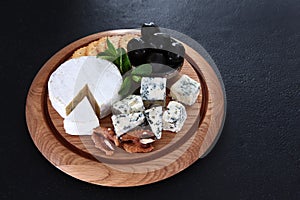 Soft cheese with white mold on a round wooden board. Camembert and blue-mildewed cheese. Cheese plate with olives and crackers.