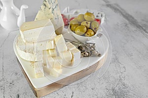 soft cheeses with white mold on a white board. A round small head of brie or camembert cheese. A set of knives and a