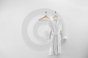 Soft comfortable bathrobe hanging on white wall, space for text