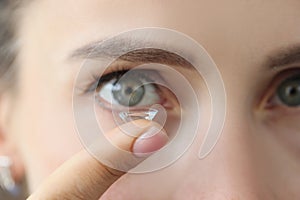 Soft contact lens on female finger against background of female eyes