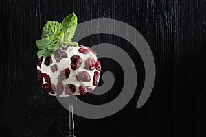 Soft dessert cheese with cranberries on a fork. Photo on a black background. Mint leaves on top. Copy of the space
