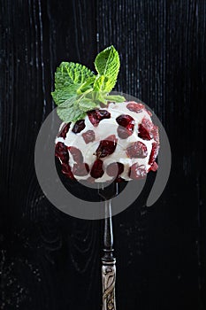 Soft dessert cheese with cranberries on a fork. Photo on a black background. Mint leaves on top. Copy of the space. Vertical photo