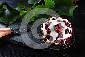 Soft dessert cheese with cranberries and grape leaves on a black background. Sweet cheese for Breakfast. Cheese knife.Delicious