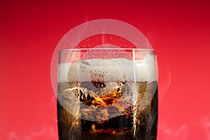 Soft drink glass with ice splash on cool smoke background. Cola glass with summer refreshment