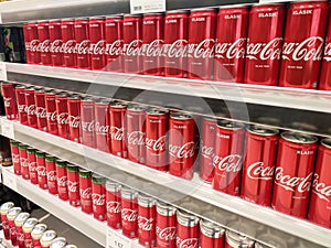 Soft drinks in cans are displayed on a shelf for sale in a large supermarket.