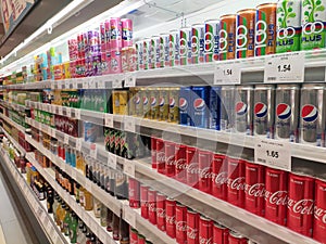 Soft drinks in cans are displayed on a shelf for sale in a large supermarket.