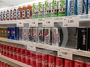 Soft drinks in cans are displayed on a shelf for sale in a large supermarket.