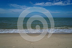 Soft foam sea wave line on white sandy beach with blue sky and white cloud background