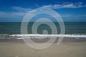 Soft foam sea wave on white sandy beach with blue sky and white cloud background