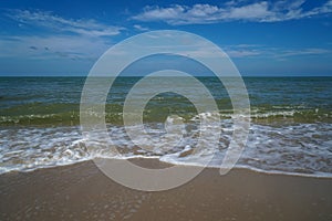 Soft foam slow sea wave on white sand beach with blue sky and white cloud background