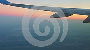 Soft focus aerial view on airplane wing above blue land and white fog against pink sky