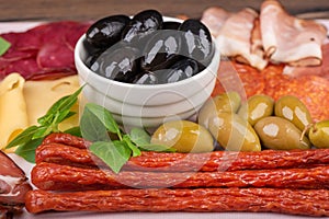Soft focus on appetizers of smoked sausages, cheese and olives.