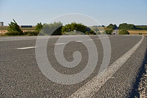soft focus asphalt road surface with white markings close-up from the low shot. blured country road and field with