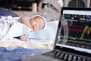 The Soft focus on baby .The parents father Stock trader trading stock on his laptop while his newborn infant baby sleep on the bed