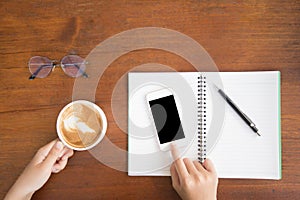 Soft focus,blur.Top view woman hands holding cup of coffee and touching mobile phone with blank copy space for your text message