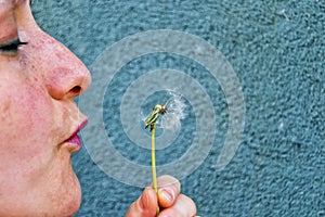 Soft focus of Caucasian white woman blowing a white dandelion flower on a green background