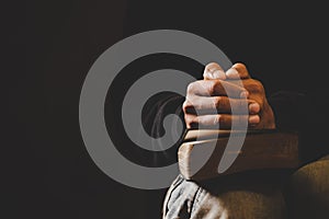 Soft focus on a hand of man while praying for christian religion with blurred of dark background