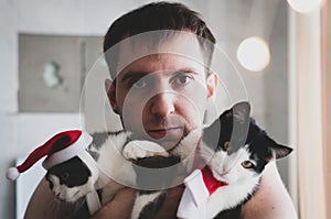 Man holding near face cute grey and white cats in christmas costums photo