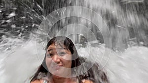 Soft focus live camera footage of a hysteric happy blogger girl swimming in a lake unser waterfall using selfie camera.