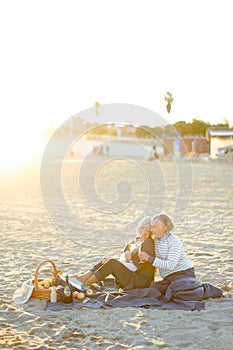 Soft focus photo of two pensioners sitting on plaid on sand beach with champagne.