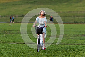 Soft focus photo. A young, beautiful blond woman with a white bike in a green meadow.