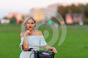 Soft focus photo. A young, beautiful blond woman with a white bike in a green meadow.