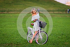 Soft focus photo. A young, beautiful blond woman with a white bike in a green meadow.