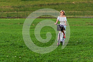 Soft focus photo. A young, beautiful blond woman with a white bike in a green meadow.