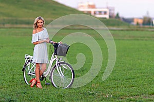 Soft focus photo. A young, beautiful blond woman with a white bike in a green meadow