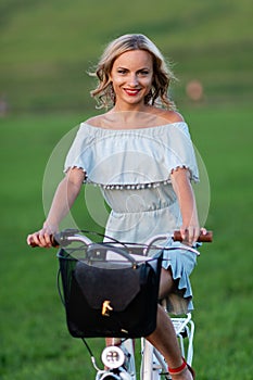 Soft focus photo. A young, beautiful blond woman with a white bike in a green meadow