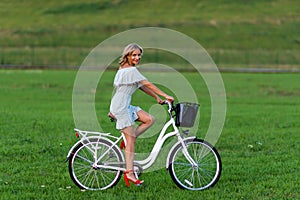 Soft focus photo. A young, beautiful blond woman with a white bike in a green meadow