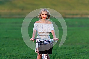 Soft focus photo. A young, beautiful blond woman with a white bike in a green meadow