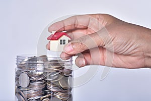 Soft focus on small house in woman's hand on the top of the coin saving bottle.