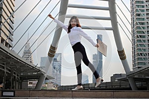 Soft focus of successful young Asian business woman raising her arms with document folder at urban building background.