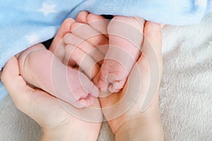 Soft focus .Tiny bare legs and feet of newborn in Mather hands. Little baby sleeps on white bed covered with blue soft