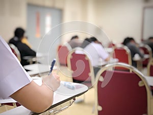 Soft focus of undergraduate student in university holding pencil writing on paper answer sheet.sitting on red lecture chair taking