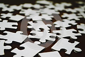 Soft focus of white jigsaw puzzle pieces on a brown surface