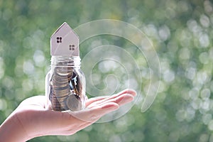 Soft focus of Woman hand holding model house on coins money in glass bottle on natural green background, Business investment and
