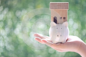 Soft focus of Woman hand holding piggy bank wth model house on natural green background, Business investment and real estate