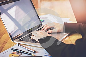 Soft focus of woman hand working laptop on wooden desk in office in morning light.