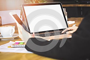 Soft focus of woman hand working with phone and laptop on wooden desk in office in morning light.