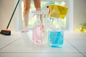 Soft focus on yellow rag with detergents, household chemicals and cleaning products against a housewife sweeping floor
