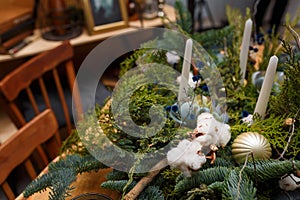 Soft focused close up shot of rustic style Christmas festive table, fresh thuja, fir, cotton branches bouquet, white candles. Eco-